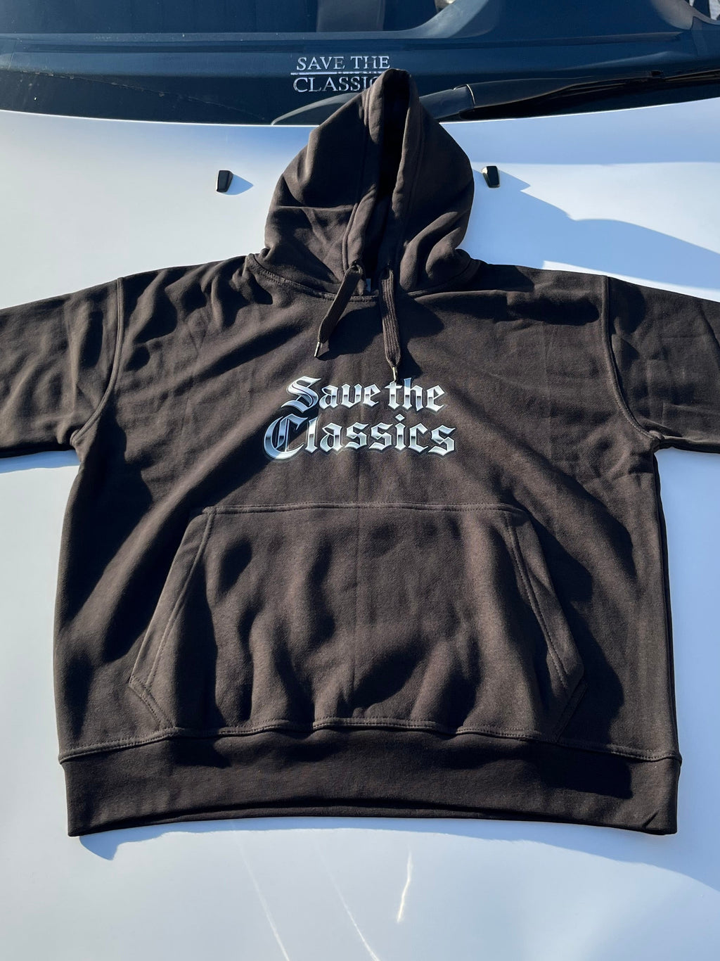 Ein schwarzer Kapuzenpullover Save The Classics von SaveTheClassics mit der Aufschrift "Save the Classics" in weißen gotischen Buchstaben ist auf der Motorhaube eines weißen Autos abgebildet, wobei derselbe Satz auf der Windschutzscheibe dahinter zu sehen ist.