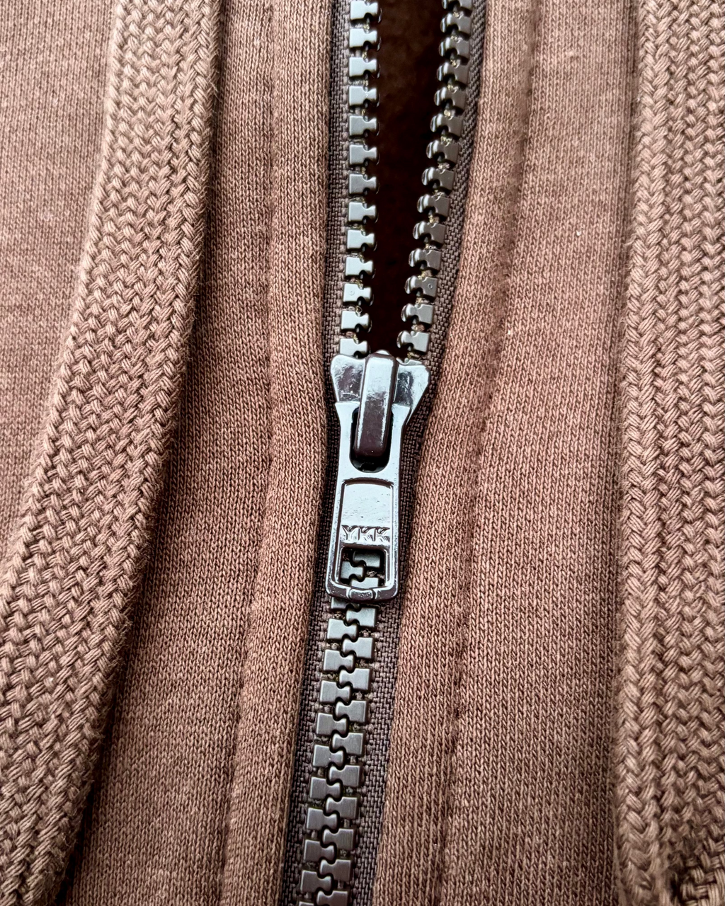 Ein brauner SaveTheClassics Zip Hoodie mit kleinem SIC-Logo auf der linken Brust liegt auf der dunkelblauen Motorhaube eines Autos und unterstreicht die automobile Streetwear mit der Windschutzscheibe und dem Innenraum im Hintergrund.