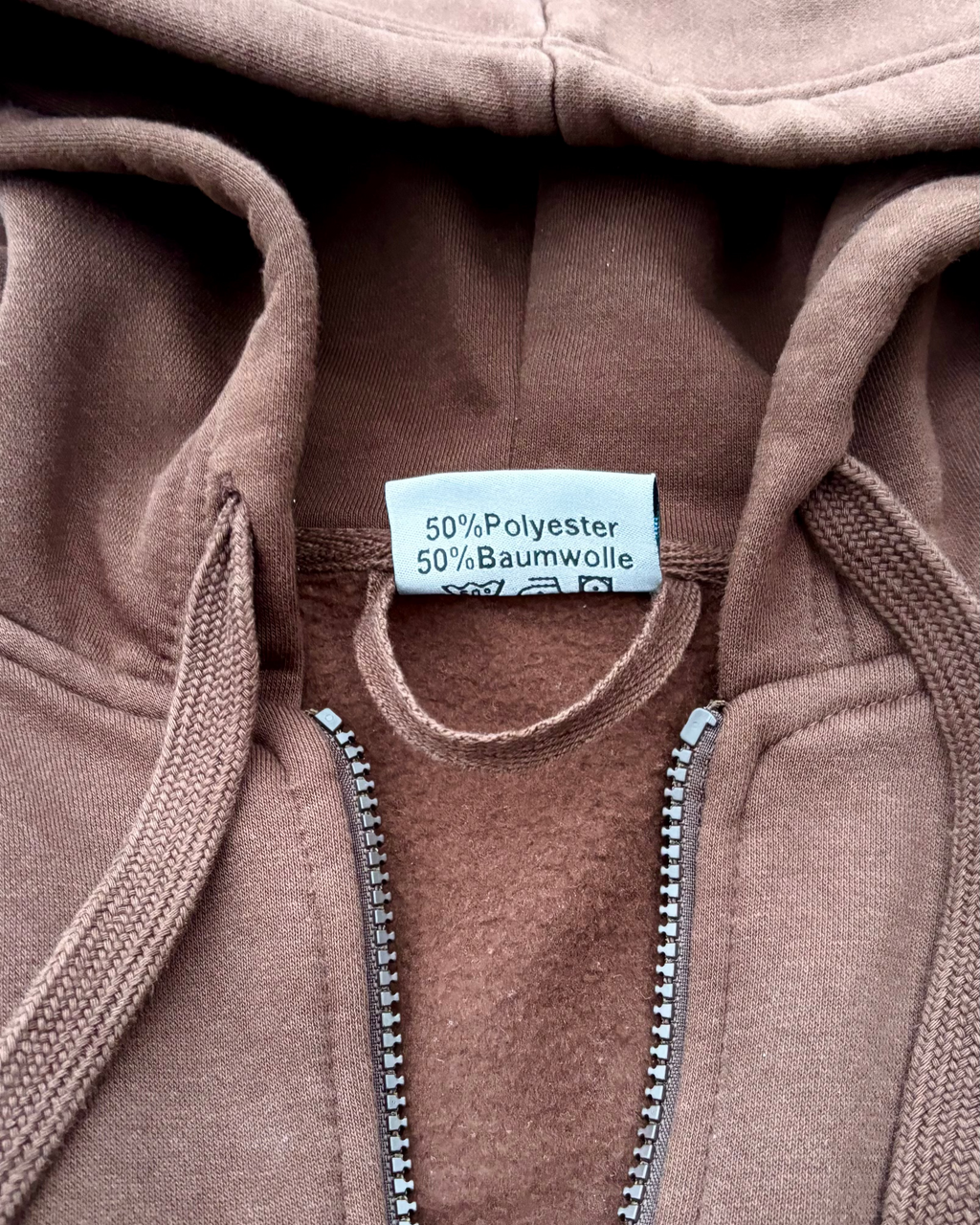 Ein brauner SaveTheClassics Zip Hoodie mit kleinem SIC-Logo auf der linken Brust liegt auf der dunkelblauen Motorhaube eines Autos und unterstreicht die automobile Streetwear mit der Windschutzscheibe und dem Innenraum im Hintergrund.